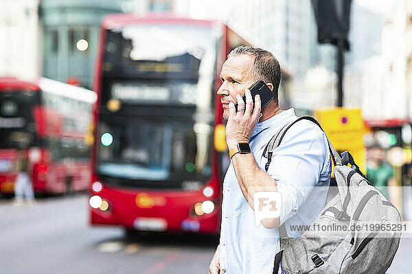 Businessman with backpack talking on smart phone at street