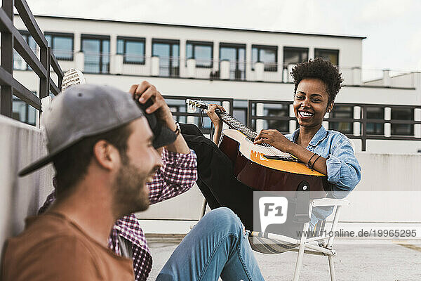 Smiling woman playing guitar near friends on terrace