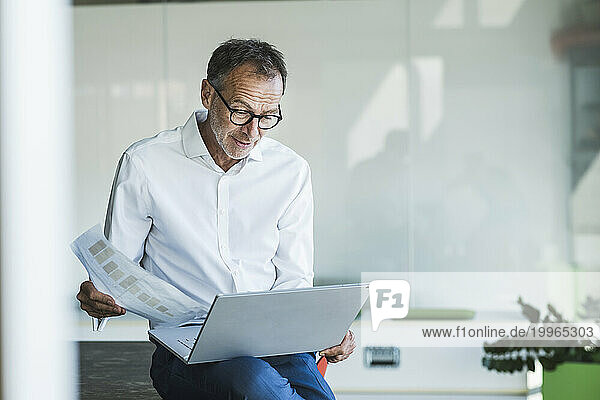 Businessman sitting with graph and using laptop in office