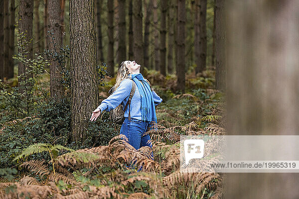Happy young woman standing with arms outstretched in Cannock chase forest