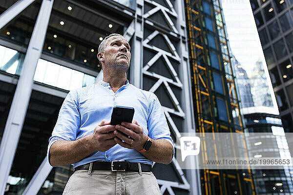 Businessman holding smart phone in front of office building