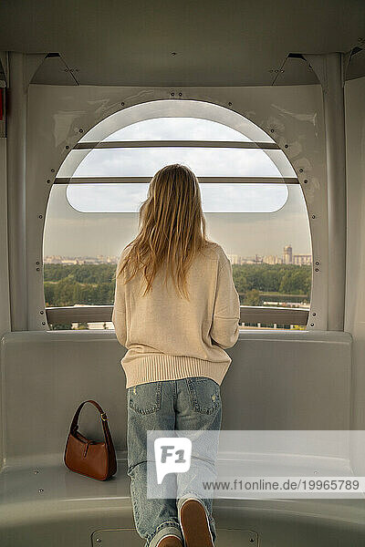 Woman kneeling on seat and looking through Ferris wheel window