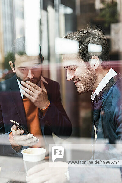 Businessman showing smart phone to colleague at cafe