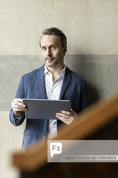 Mature businessman with tablet PC in front of wall