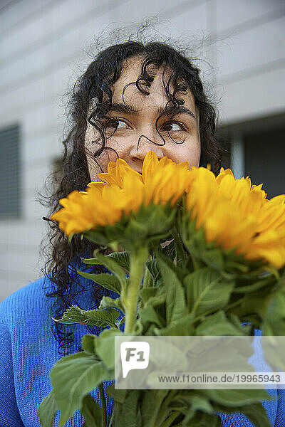 Young woman with curly hair smelling sunflowers