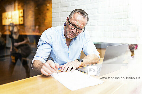 Businessman writing on document near laptop at cafe