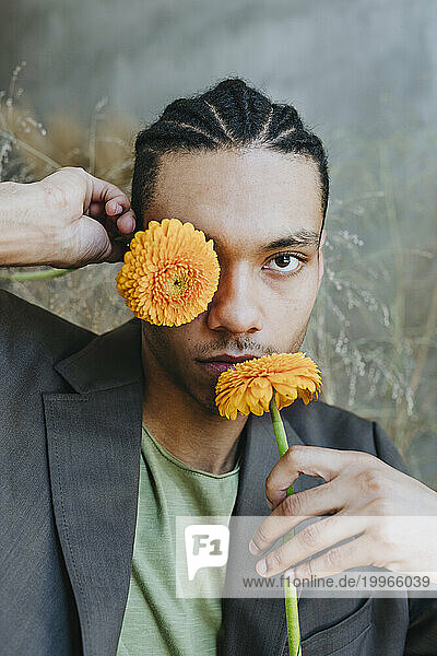 Businessman holding Gerbera flowers over face in garden