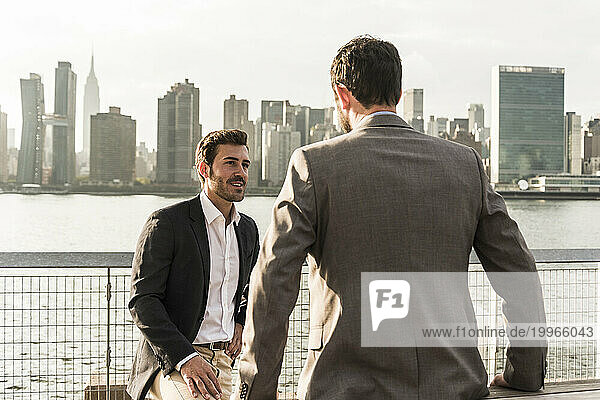 Smiling businessman talking to colleague by Hudson river in New York City  USA