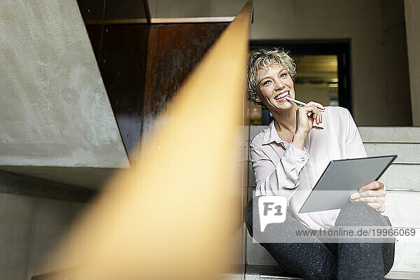 Happy businesswoman with tablet PC sitting on staircase