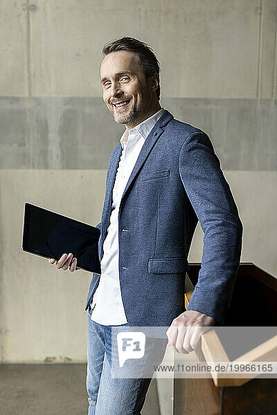 Smiling mature businessman with tablet PC by wall