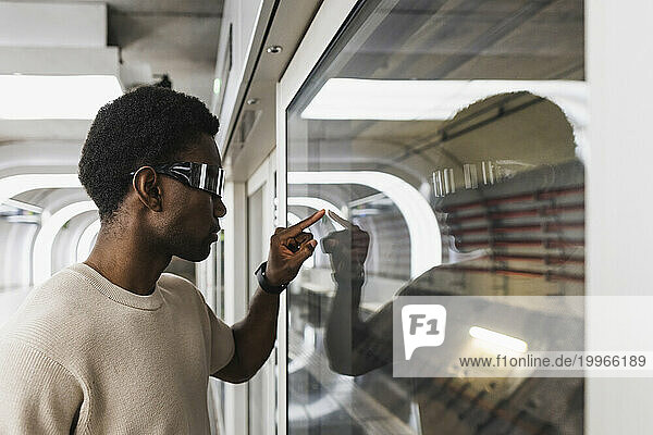 Young man with cyber glasses touching glass pane with his forefinger