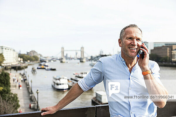 Smiling businessman talking on smart phone in London  UK