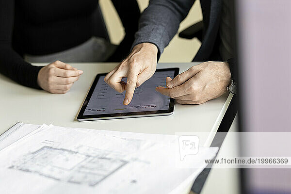 Businessman using tablet PC with trainee at desk in workplace