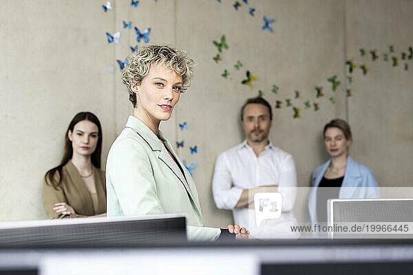 Confident businesswoman with colleagues in background at office
