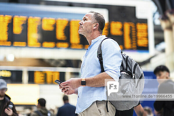 Businessman with backpack holding smart phone at station