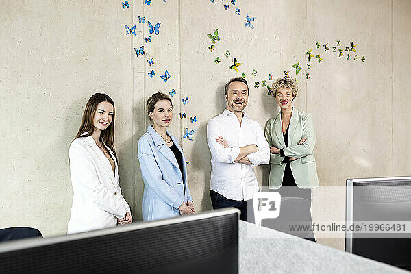 Smiling colleagues standing in front of wall with butterflies stickers at office