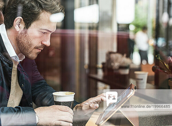 Young businessman with coffee cup using tablet PC at cafe