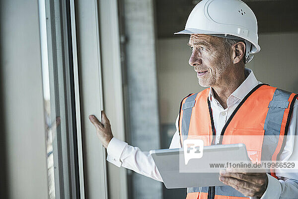 Engineer holding tablet PC and looking through window