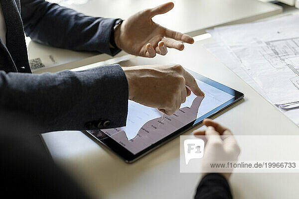 Hand of businessman using tablet computer by trainee at desk in office