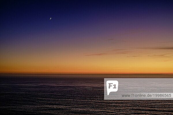 Schöne ruhige Blick auf den Ozean bei Sonnenuntergang  mit einem Farbverlauf von orange bis lila und eine Mondsichel in den Himmel. Bunte klaren Himmel in der Dämmerung  Horizont über Wasser  ruhige Gewässer. Meereslandschaft im Hintergrund