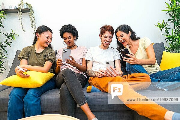 Frontalansicht multiethnischer Freunde  die zu Hause auf dem Sofa sitzen und ein Handy benutzen