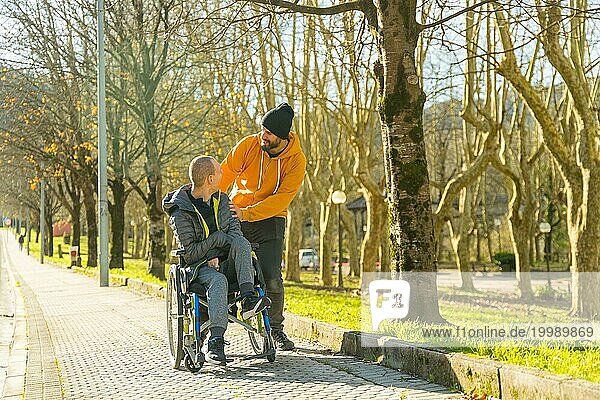 Mann  der den Rollstuhl eines behinderten Freundes auf dem Weg durch einen Park schiebt