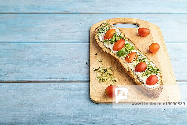 Langes Weißbrot Sandwich mit Frischkäse  Tomaten und Mikrogrün auf blauem Holzhintergrund. Seitenansicht  Kopierraum