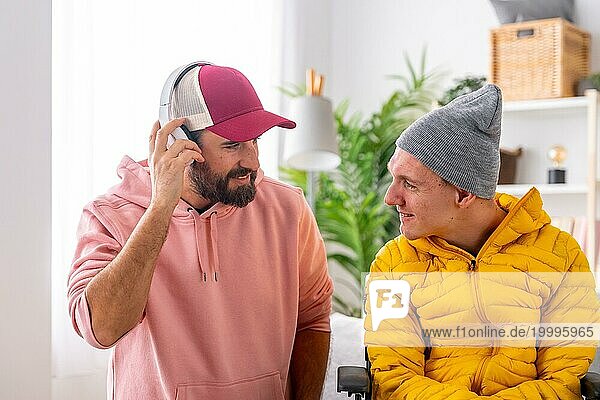 Mann hört mit Kopfhörern neben einem behinderten Freund im Rollstuhl zu Hause Musik