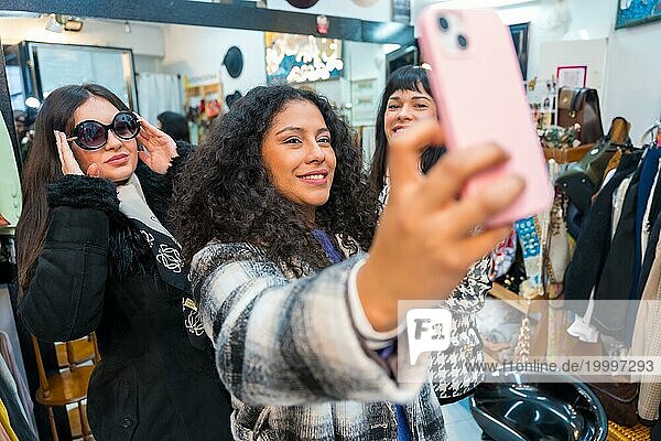 Frontalansicht von drei weiblichen Schönheiten  die ein lustiges Selfie machen  während sie im Verkauf Kleider anprobieren