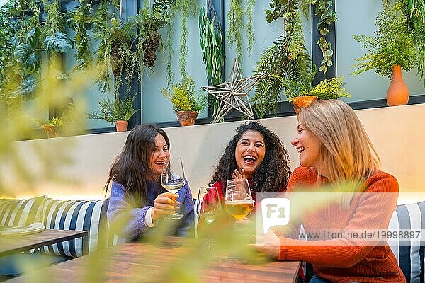 Im Mittelpunkt stehen drei erwachsene Frauen  die sich in einer Cafeteria beim Weintrinken amüsieren