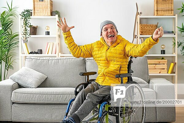 Glücklicher und ausdrucksstarker behinderter Mann im Rollstuhl  der zu Hause die Hände vor Freude hebt