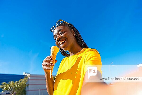 Afrikanische Frau  die ein Selfie macht  während sie an einem sonnigen Tag draußen in der Stadt Eis isst