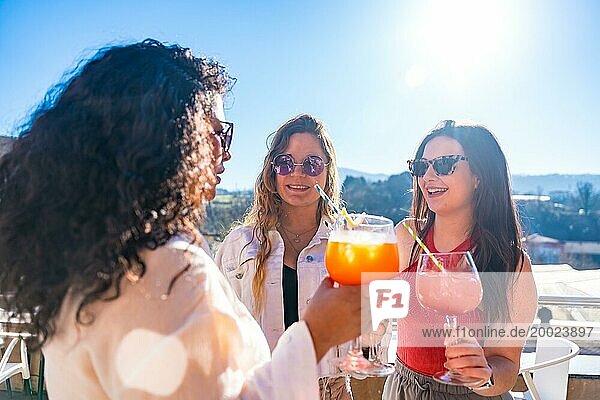 Drei coole Freundinnen stoßen an einem sonnigen Tag mit Cocktails auf einer Dachterrasse auf den Sommer an