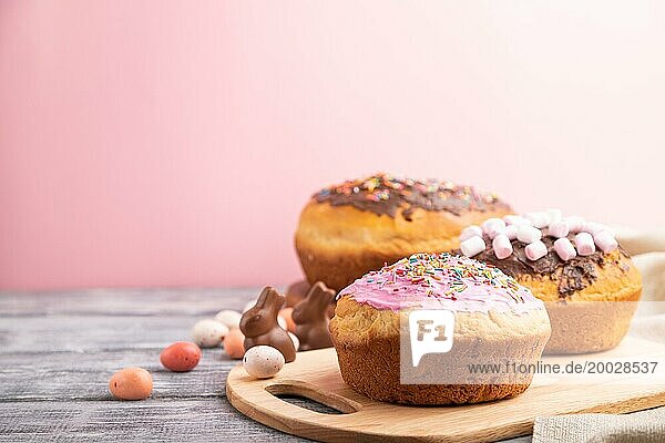 Hausgemachte glasierte und dekorierte Osterkuchen mit Schokoladeneiern und Kaninchen auf grauem und rosa Hintergrund und Leinenstoff. Seitenansicht  selektiver Fokus  Kopierraum