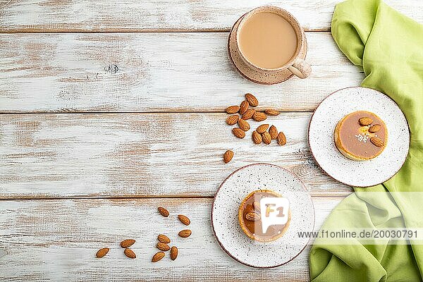 Süße Törtchen mit Mandeln und Karamellcreme mit einer Tasse Kaffee auf weißem Holzhintergrund und grünem Textil. Draufsicht  Flat Lay  Copy Space