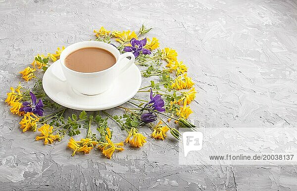 Gelbe und blaue Blumen in einer Spirale und eine Tasse Kaffee auf einem grauen Betonhintergrund. Morninig  Frühling  Mode Zusammensetzung. Seitenansicht  Kopie Raum