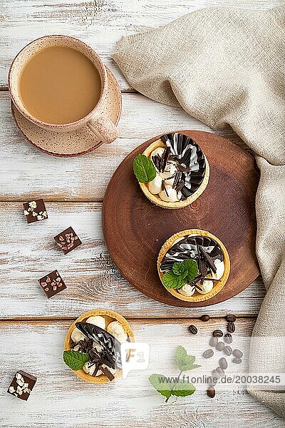 Süße Törtchen mit Schokolade und Käsecreme mit einer Tasse Kaffee auf weißem Holzhintergrund und Leinentextil. Draufsicht  Flachlegung  Nahaufnahme