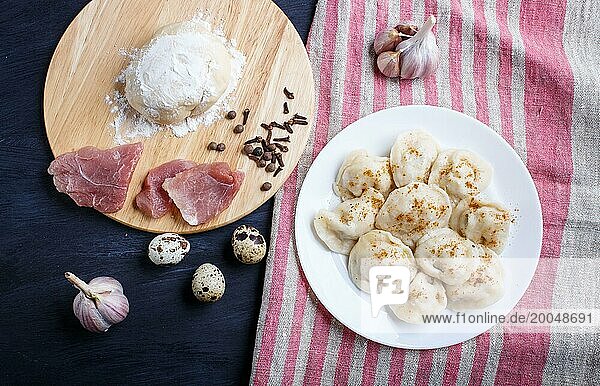 Dumplings on a plate with ingredients (meat  dough  spices) on a linen tablecloth on a black wooden background. top view  flat lay