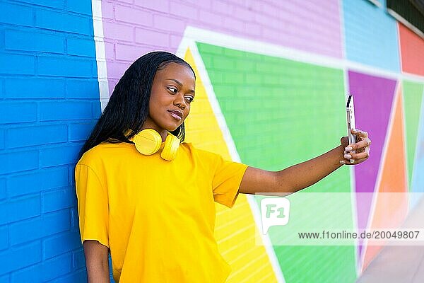 Seitenansicht Porträt einer jungen afrikanischen Frau posiert ein Selfie lehnt an einer bunten Wand