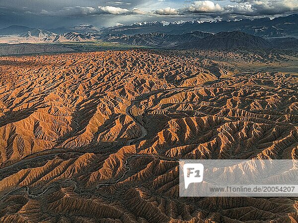 Landscape of eroded hills  badlands at sunset  mountain peaks of the Tian Shan Mountains in the background  aerial view  Canyon of the Forgotten Rivers  Issyk Kul  Kyrgyzstan  Asia