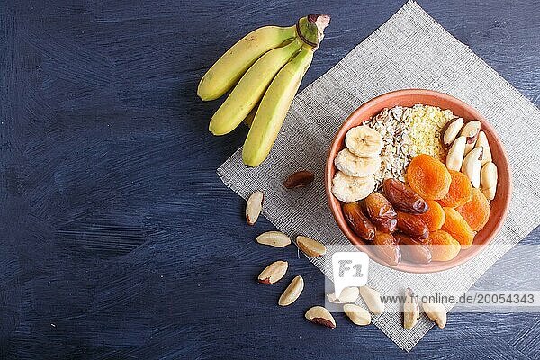 A plate with muesli  banana  dried apricots  dates  Brazil nuts on a black wooden background. top view. copy space