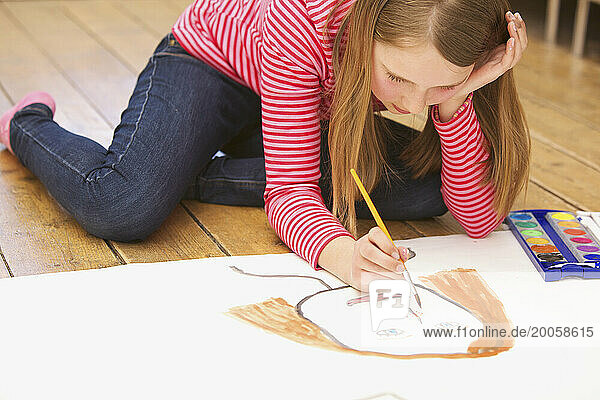Girl kneeling on floor painting with watercolors