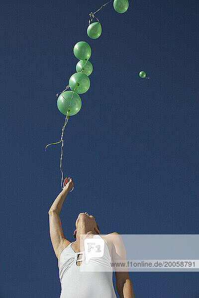 Woman releasing green balloons in a cloudless sky - low angle view