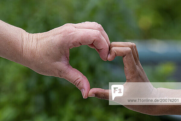 Mixed race mum and son playing in the garden bonding  laughing together making a heart sign. Uncondition love