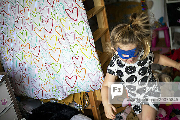 Young girl running around with face mask and costume on  playing superhero with her sister