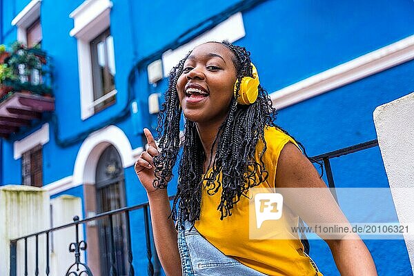 African woman singing to the camera and dancing in the street next to a blue house