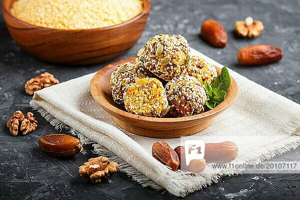 Energy ball cakes with dried apricots  sesame  cornflakes  linen  walnuts and dates with green mint leaves in a wooden bowl on a black concrete background. linen napkin  side view  close up  selective focus  vegan homemade candy