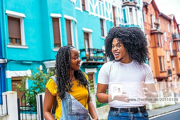 Zwei glückliche junge afrikanische Freunde unterhalten sich beim Besuch einer Straße mit bunten Häusern