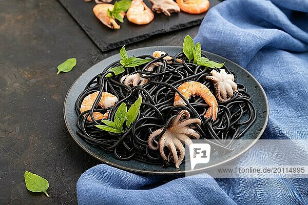 Black cuttlefish ink pasta with shrimps or prawns and small octopuses on black concrete background and blue textile. Side view  close up