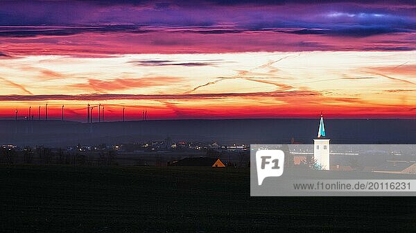 Glockenturm bei Sonnenaufgang mit Windrädern beleuchtet